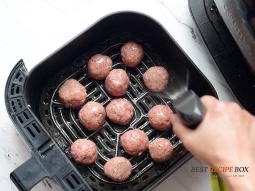 oil spray on raw meatballs in air fryer basket