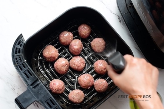 oil spray on raw meatballs in air fryer basket