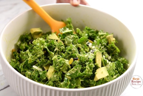 Kale salad being tossed with raisins and nuts