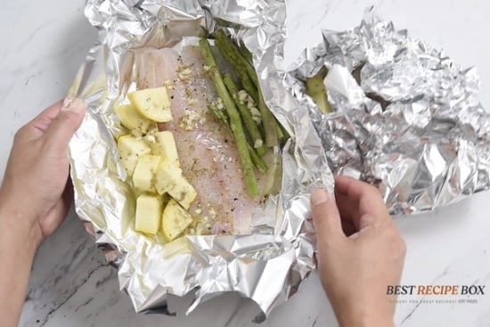 Folding the foil over the fish fillet with the veggies and garlic butter mixture