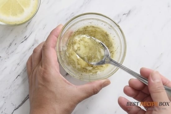 Spoonful of garlic butter mix above bowl