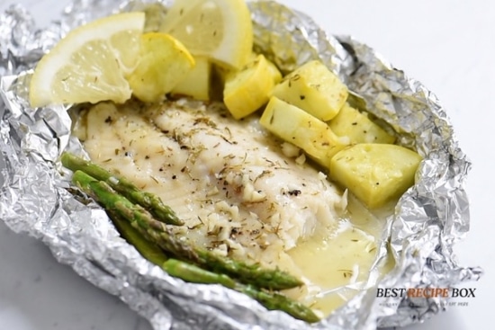 Cooked tilapia fillet in foil pack with veggies and bite taken out of it