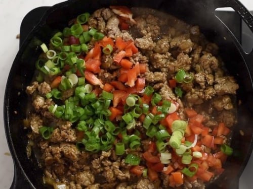 Green onions and bell peppers added to cooked ground turkey in a skillet