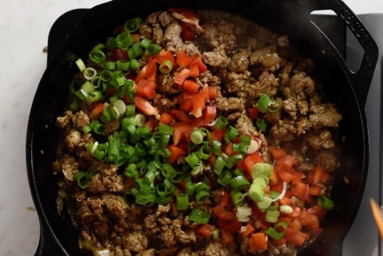 Green onions and bell peppers added to cooked ground turkey in a skillet
