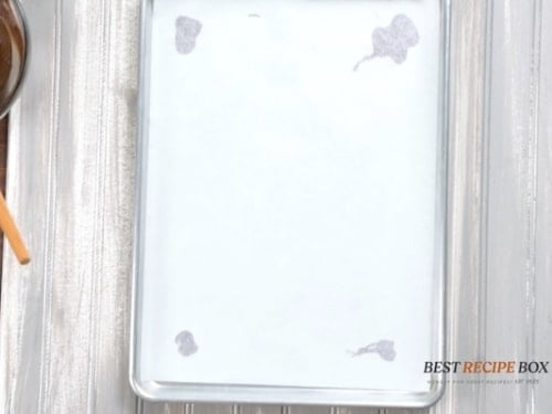 Parchment lined baking sheet pan secured by melted chocolate dots