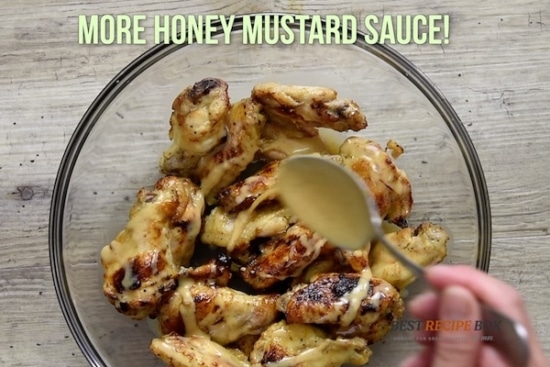 Cooked chicken wings in bowl with more sauce being poured over with a spoon