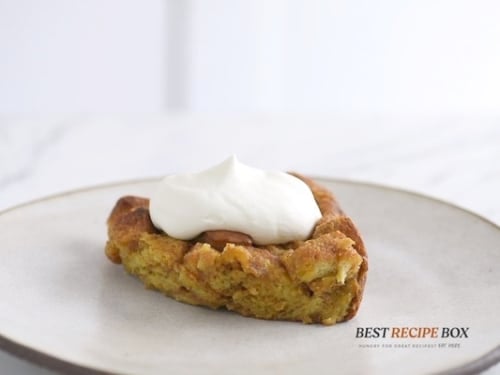 Piece of pumpkin bread pudding topped with whipped cream on a plate