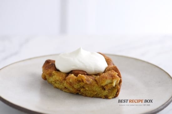 Piece of pumpkin bread pudding topped with whipped cream on a plate
