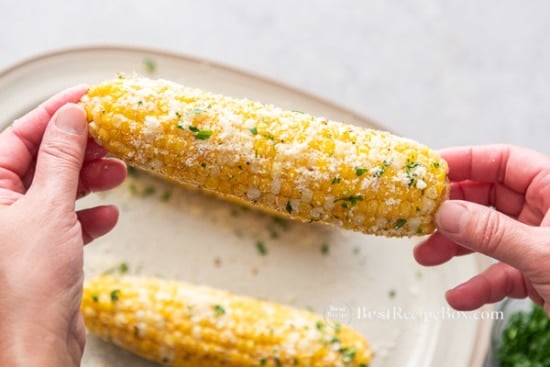 Holding up the corn coated with parmesan