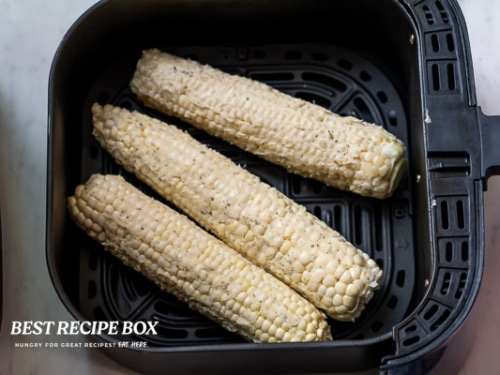 Uncooked corn on the cobs in air fryer basket