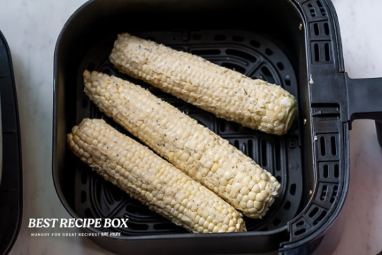 Uncooked corn on the cobs in air fryer basket