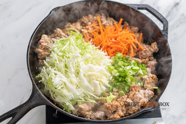 Adding cabbage and carrots to cooked chicken
