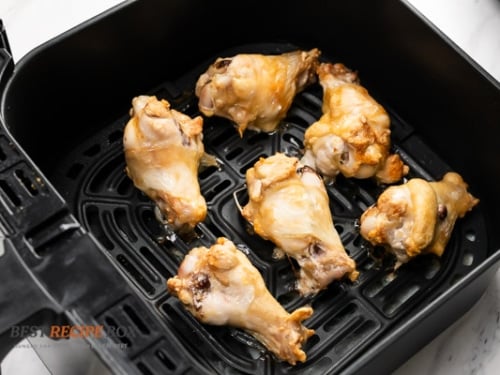 Half cooked chicken wings in air fryer basket