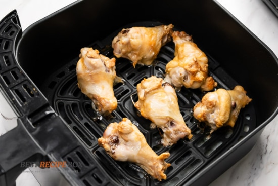 Half cooked chicken wings in air fryer basket