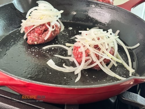 sliced onions on top of beef burger patty