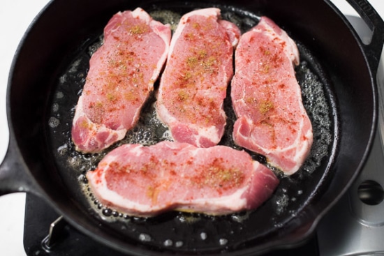 Pork chops being seared in a skillet