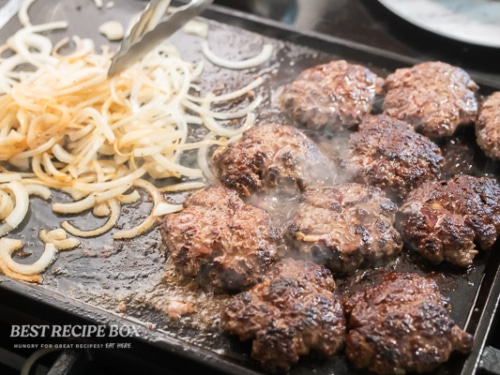 sliders and onions cooking on flat top