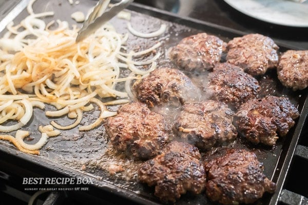 sliders and onions cooking on flat top