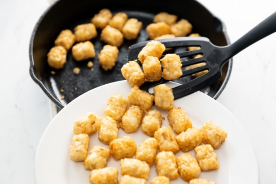 lifting tater tots out of a skillet with a spatula